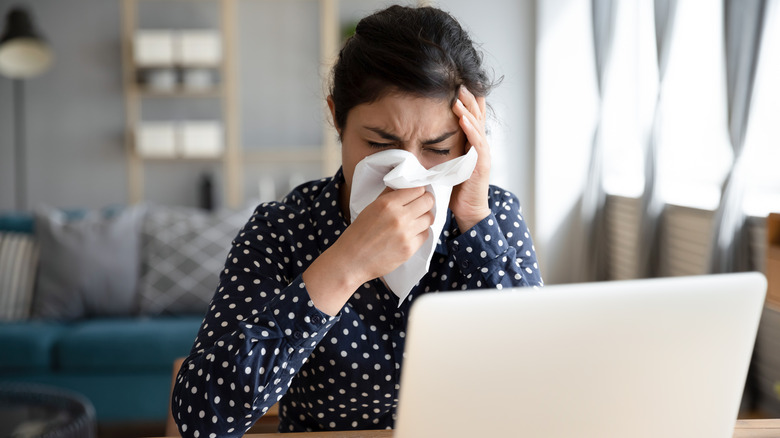 Woman on computer blowing her nose