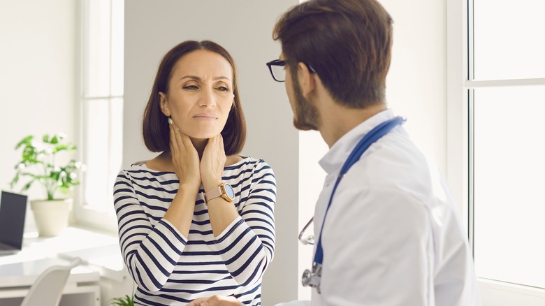 Woman holding throat in pain talking with doctor