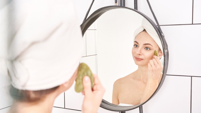 woman using gua sha tool in mirror