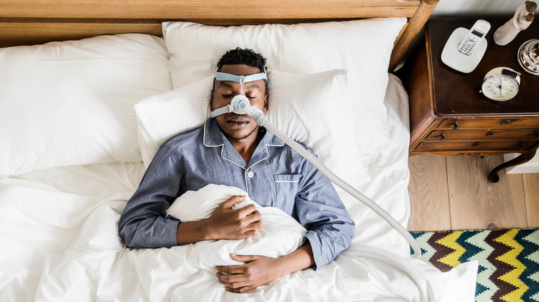 Man asleep in bed with sleep apnea breathing machine on his face
