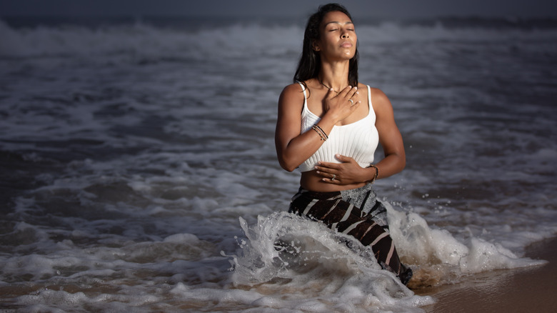 Thara Natalie sits in the water holding one hand on her chest and one hand on her stomach