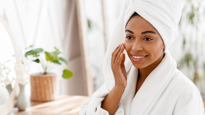 young woman in a white robe looking satisfied with her skin