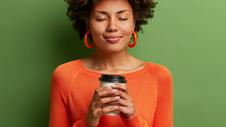 Calm, smiling woman holding coffee/tea to-go cup