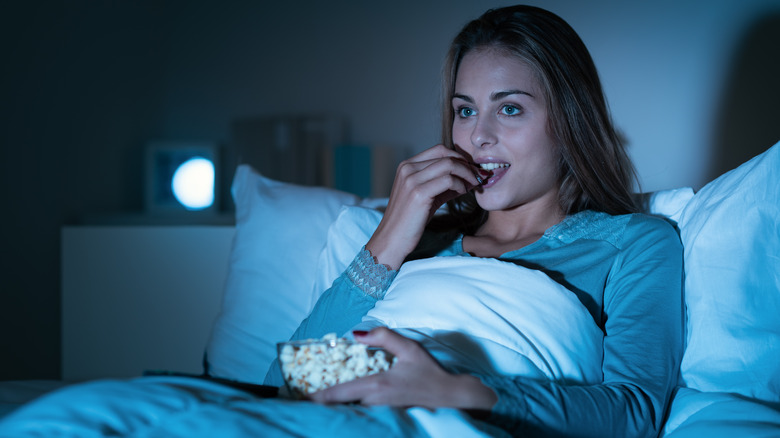 woman eating popcorn and watching tv in bed