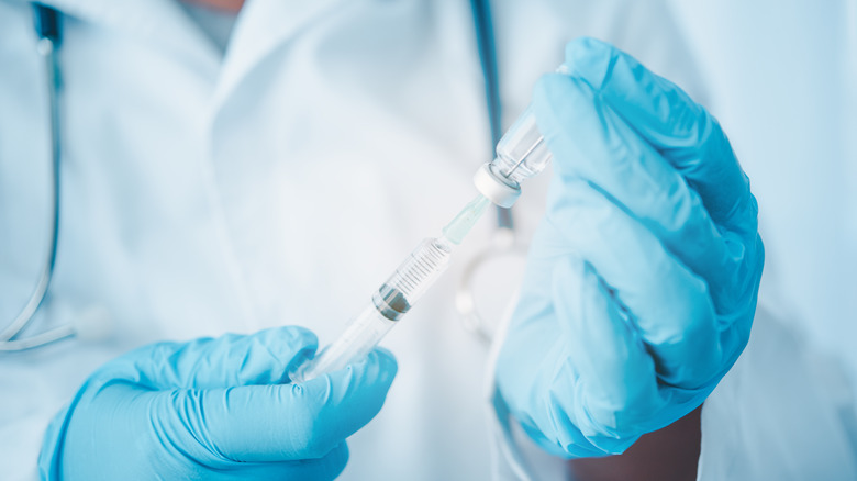 Doctor's hands in pale blue gloves drawing preparing a vaccine syringe.