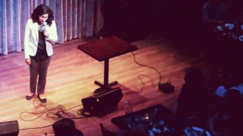 Wide shot of Priyanka standing on a stage with a microphone