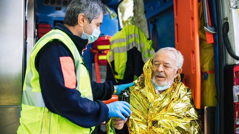An older man in a warming blanket with an emergency worker