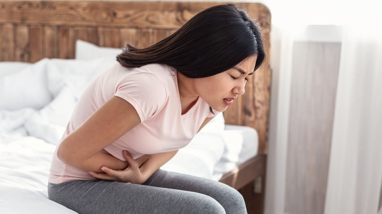 Woman sitting hunched over on a bed, holding her stomach.