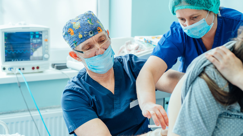 Doctors inserting catheter in patient's back for epidural