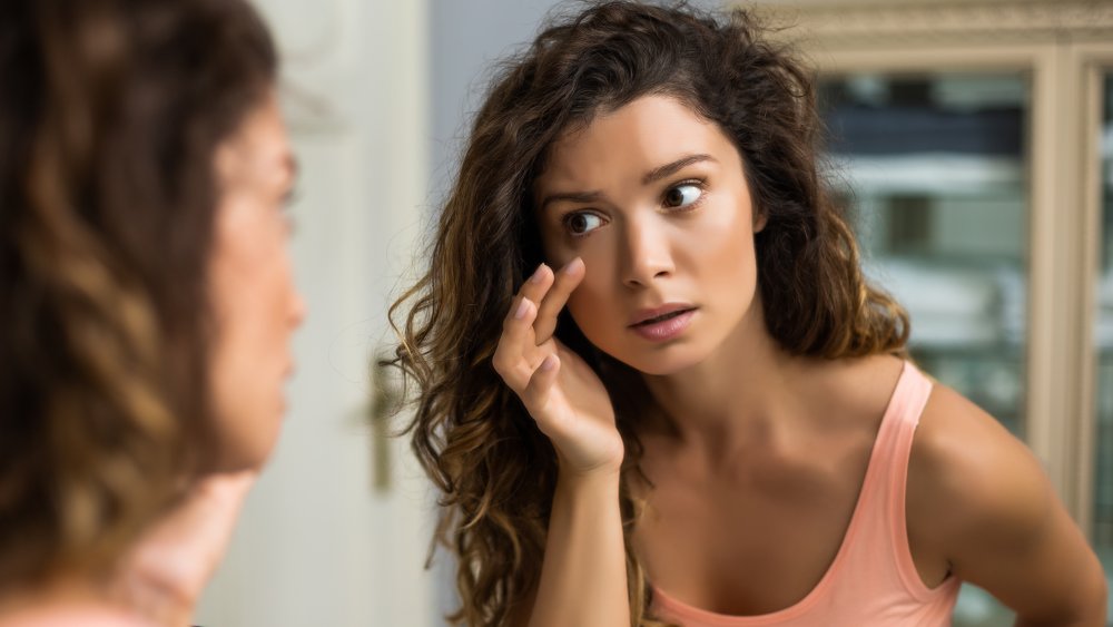 Tired woman looking in bathroom mirror