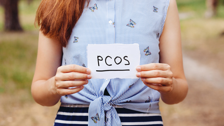 A woman holds a sign that says "PCOS"