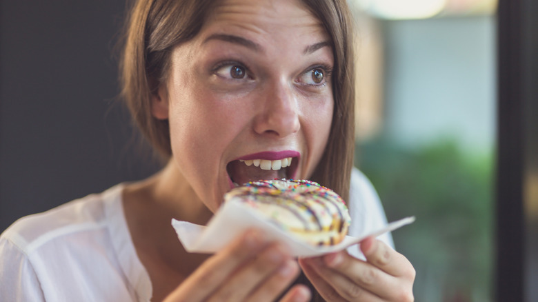 woman eating candy sprinkled donut