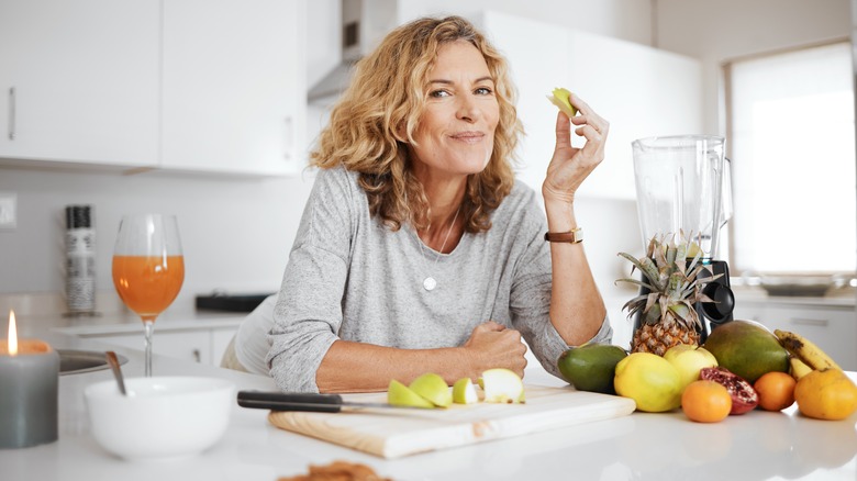 smiling woman eating fruit in kitchen