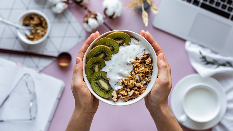 Hands holding healthy breakfast bowl over work table