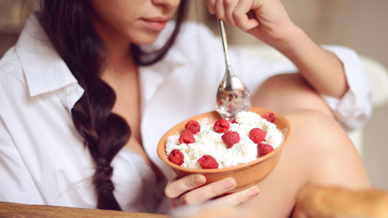 woman's hands holding a bowl of cottage cheese with strawberries