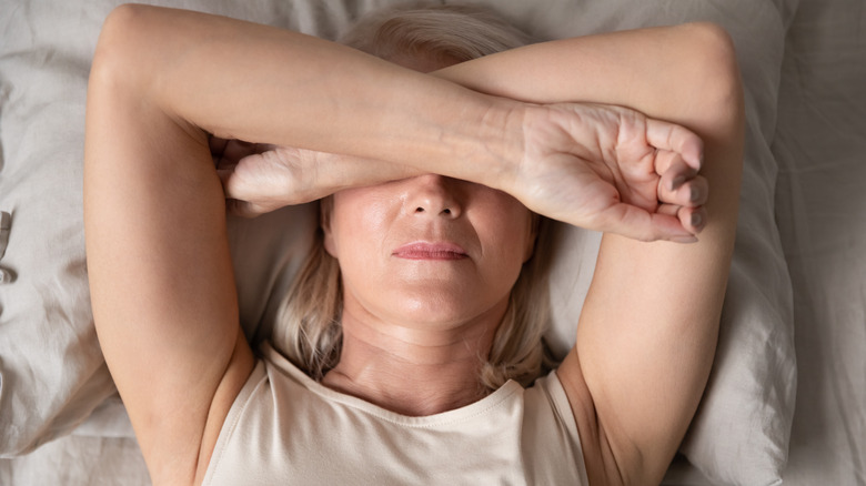 a woman in bed folds her arms over her eyes