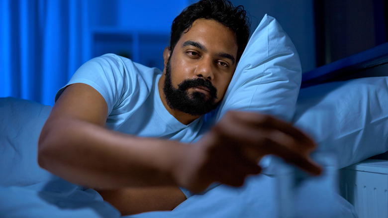 man in bed reaching for glass of water 