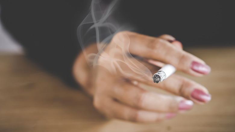 A manicured hand holding a cigarette