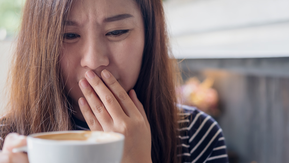 A woman holding a cup of coffee looking put off 