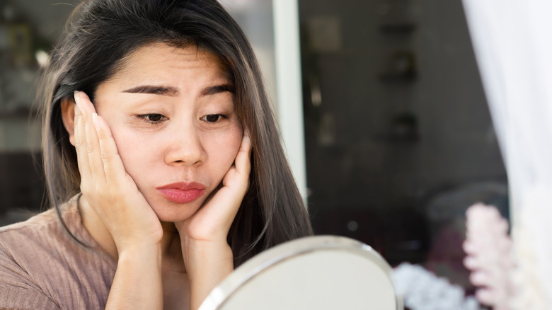 Woman with a swollen face looking in mirror