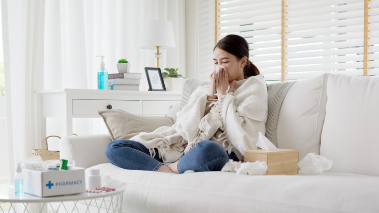 Woman sitting on sofa under a blanket and blowing nose