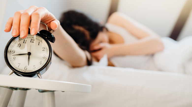 Sleeping woman turning off alarm clock