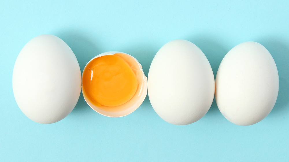 Eggs in a row with one cracked open showing the yolk