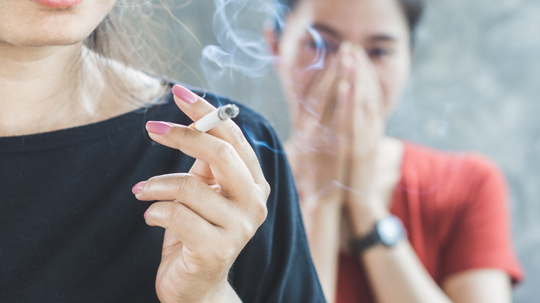 woman stands behind cigarette smoker