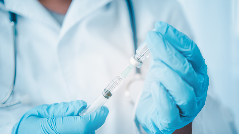 Gloved hands holding vaccine vial and syringe