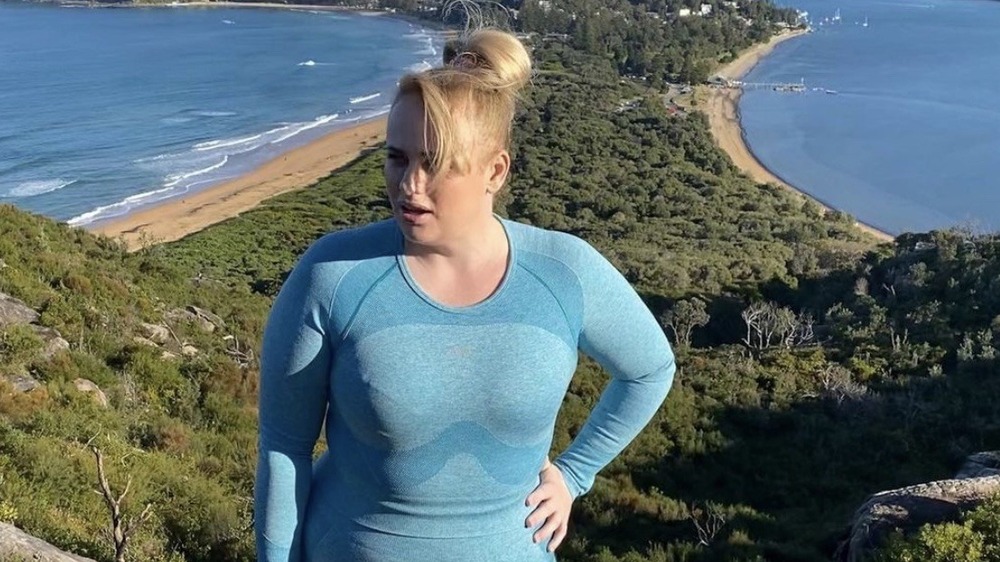 Rebel Wilson posing on top of an oceanside mountain