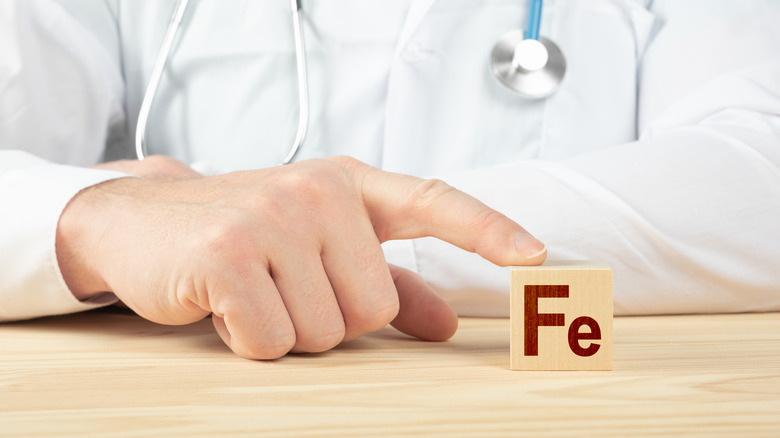 A doctor holds a block that reads "Fe"