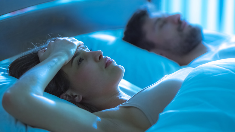 woman awake in bed next to sleeping man