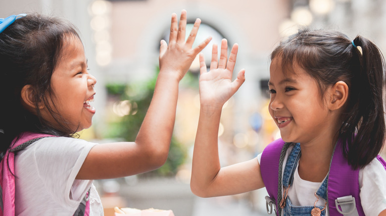 Twin girls wearing backpacks smile and high five each other