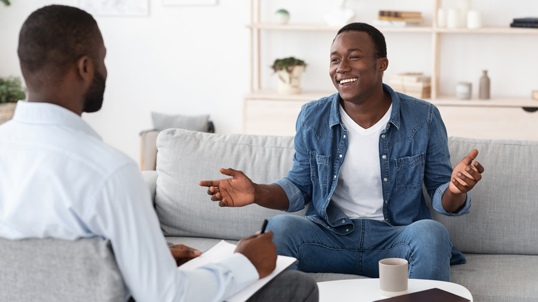Man sits happily on a couch talking to his therapist