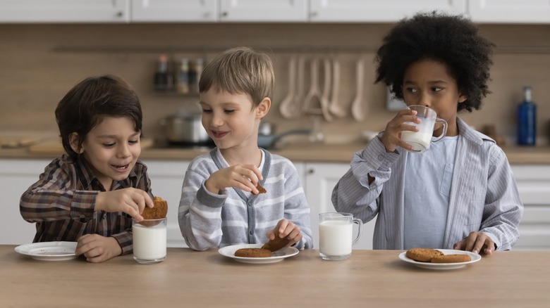 three children enjoying milk and cookies