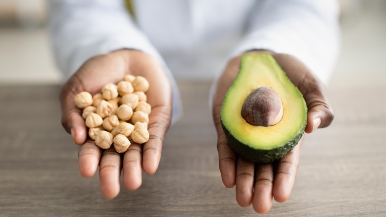 two hands holding nuts and avocado