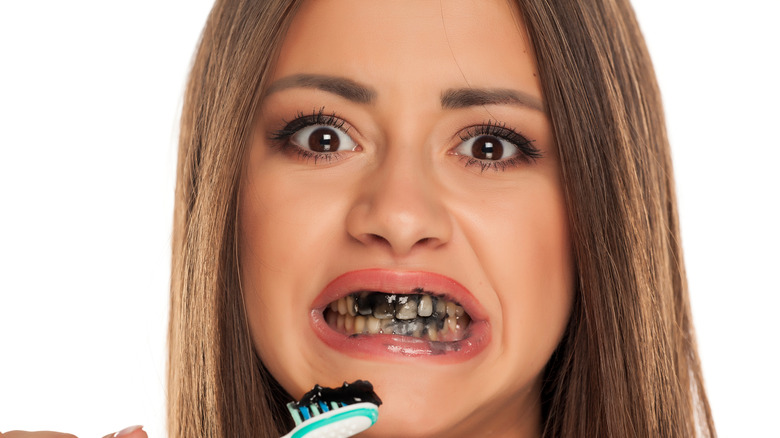 Woman making a disgusted expression with charcoal toothpaste covering her teeth