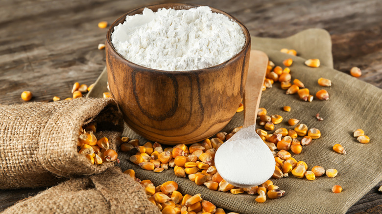 Cornstarch in wooden bowl with spoon and corn kernels