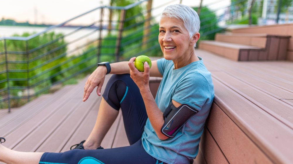 Gray haired woman in sport clothes holding a green apple