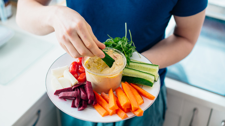 A man is dipping vegetables into hummus