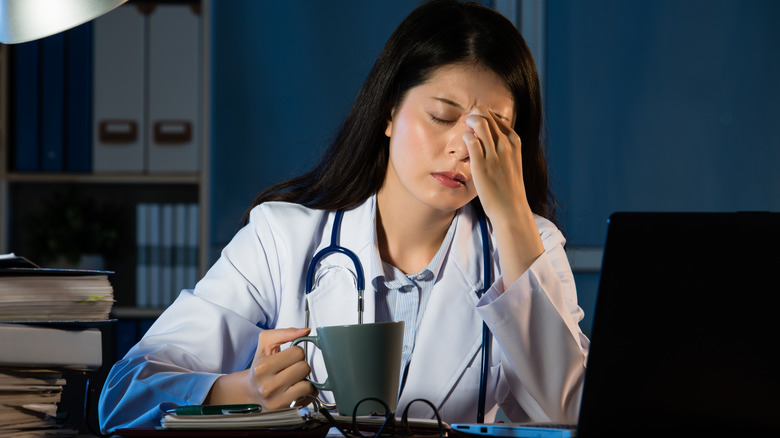 Tired doctor sitting at desk with coffee overnight