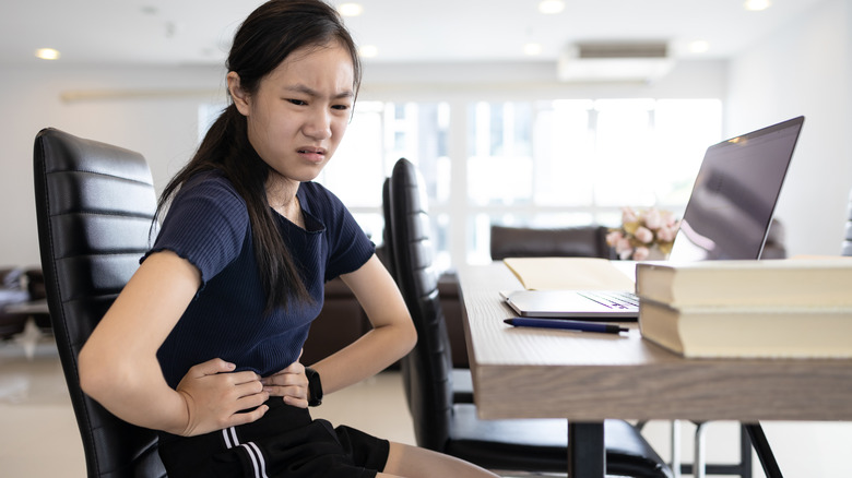 Young girl sitting at desk holding stomach in pain