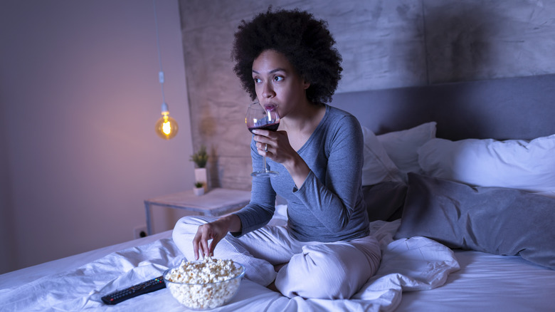 woman drinking wine and eating popcorn in bed