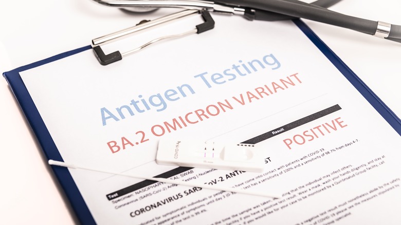 Paperwork on clipboard reading "Antigen Testing BA.2 OMICRON VARIANT: POSITIVE"