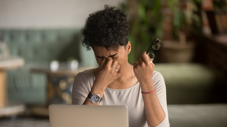 A woman sitting at a computer and pinching her eyes