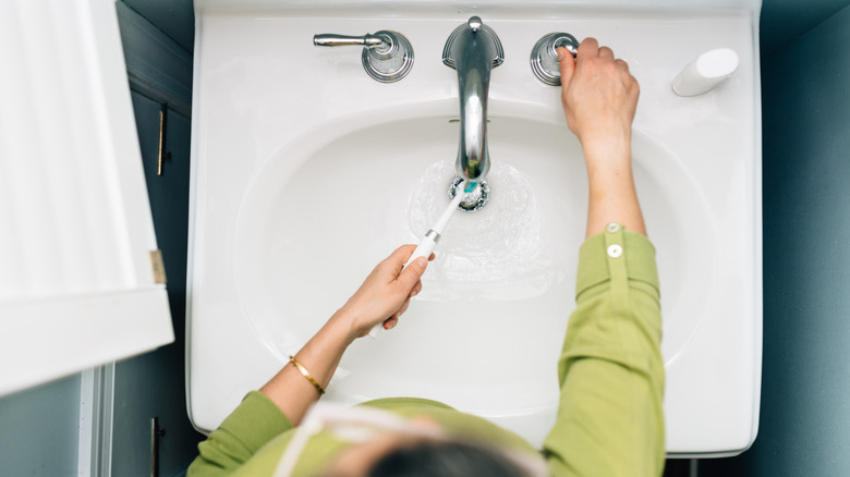 Pair of hands rinsing toothbrush in sink