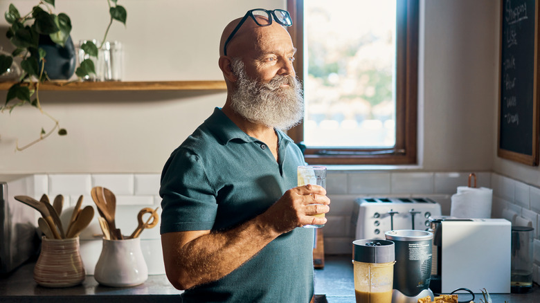 healthy older man drinking a smoothie in the kitchen