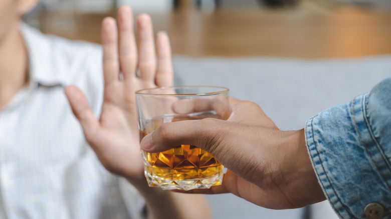 Person with their hand up refusing a glass of liquor