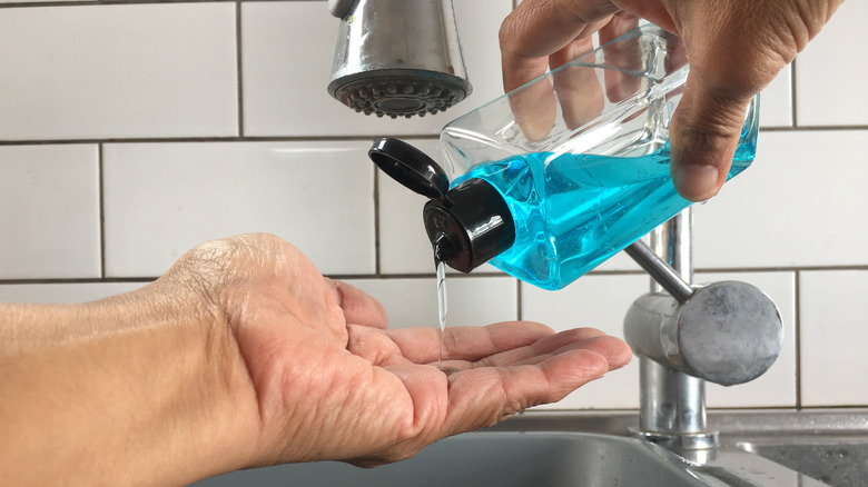 Hands under sink pouring blue liquid soap into left hand