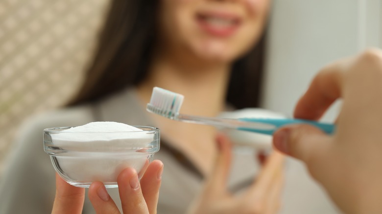 Smiling person holding baking soda and toothbrush